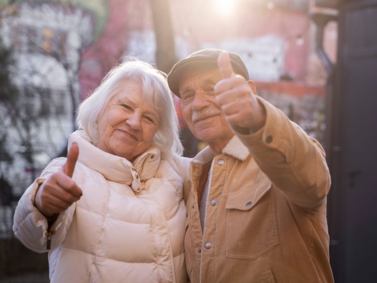 An elderly couple hugging and holding up their thumbs.